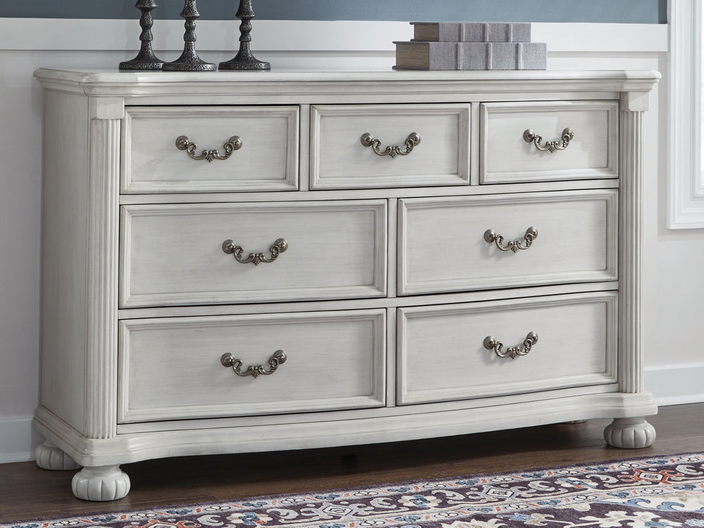 Transform your inner sanctum into a haven of timeless elegance and functionality. This traditionally styled dresser is adorned in a classic antiqued white finish, highlighted by a serpentine-shaped front with thick decorative moulding. Its drawers are pac