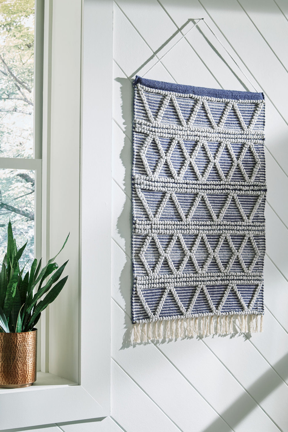 With boho-chic design in mind, this woven wall hanging adds eye-catching texture to your living space. Its diamond design, decorative fringe trim and shades of blue and gray will add interest to your wallscape, inside or out.<br/><br/><b>Product Features<