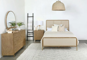 This coastal-inspired bedroom set blends mid-century modern influences with natural textures for a serene retreat. The bed features a cream fabric upholstered headboard and footboard, framed by a wire-brushed wood finish that enhances the beauty of rubber