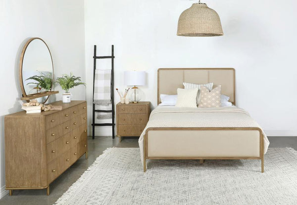 This coastal-inspired bedroom set blends mid-century modern influences with natural textures for a serene retreat. The bed features a cream fabric upholstered headboard and footboard, framed by a wire-brushed wood finish that enhances the beauty of rubber