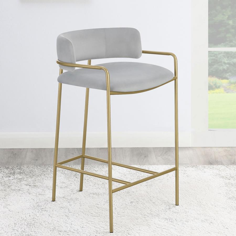 A soft and supple grey velvet envelops the comfy padded seat and linear backrest of this chic and glamorous stool. Situated and supported by a slim rod-like frame in a gold finish, this stool offers an air of sophistication to any bar top or kitchen islan