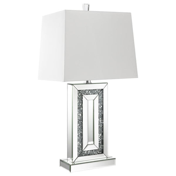 This modern table lamp features a rectangular base framed with beveled mirrored panels and sparkling crushed acrylic crystal inlay. Its geometric design delivers bold symmetry and a touch of glamour, anchored by a crisp white shade that softens the light.