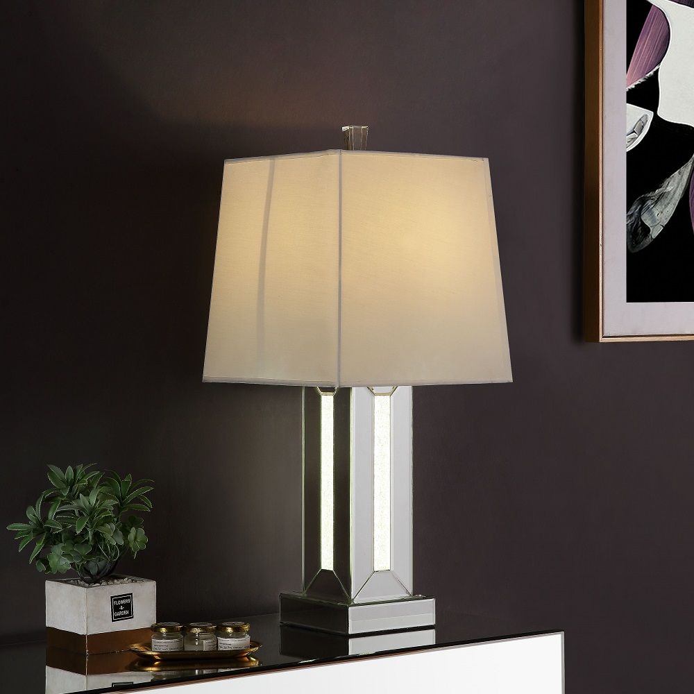 Brighten up your room in sophistication style with this Noralie Table Lamp. Fitting in a variety of design aesthetic, this piece features a classic drum shaped shade. The table lamp showcases a cuboid mirrored base with clear glass and faux stones inlayed
