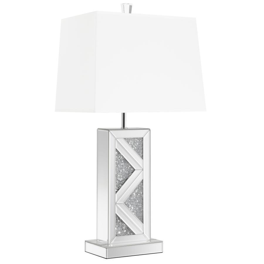 This statement-making table lamp features a rectangular base adorned with mirrored paneling and a bold chevron design inlaid with crushed crystal acrylic. A crisp white shade balances the shimmering base with a clean, structured silhouette. The geometric 