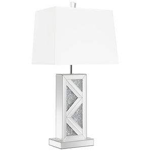 This statement-making table lamp features a rectangular base adorned with mirrored paneling and a bold chevron design inlaid with crushed crystal acrylic. A crisp white shade balances the shimmering base with a clean, structured silhouette. The geometric 
