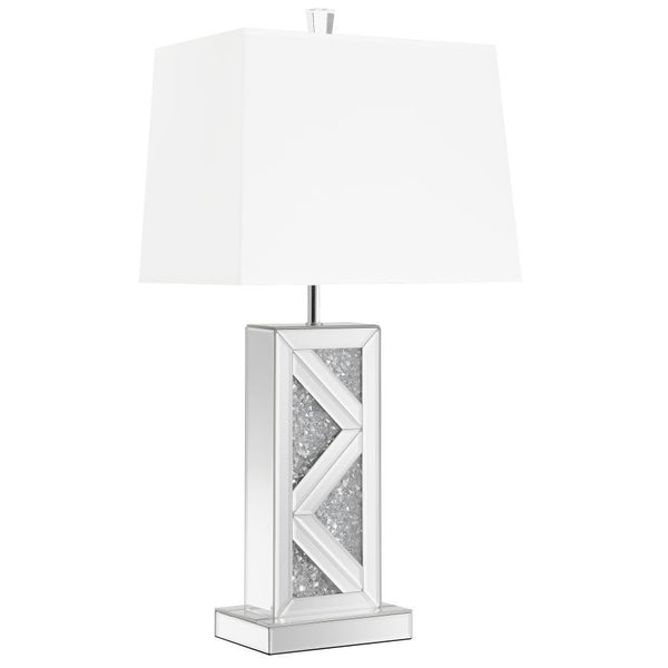 This statement-making table lamp features a rectangular base adorned with mirrored paneling and a bold chevron design inlaid with crushed crystal acrylic. A crisp white shade balances the shimmering base with a clean, structured silhouette. The geometric 