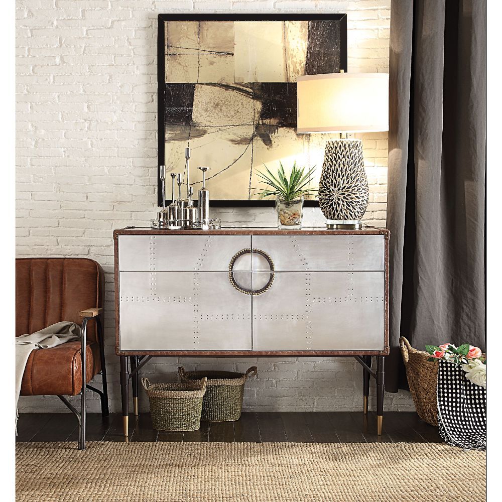 With its riveted patchwork of polished aluminum, the Brancaster console table is inspired by mid-20th-century air travel. This unique console piece features ample storage with two drawers and cabinet space with two doors, all supported by tapered metal le