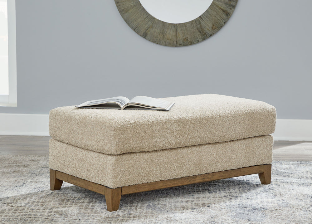 Serene style with a modern sensibility. Delight in the cozy, versatile embrace of this ottoman. It takes an on-trend approach to irresistible texture and natural beauty, showcasing soft upholstery accented with a transitional wood trim. As refined as it i
