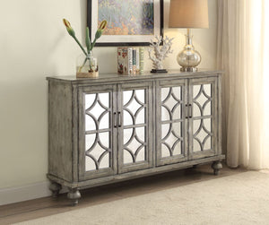 The transitional Velinka Console Table features a weather gray finish with mirrored glass doors and a diamond trim inlay. Four cabinet doors open on the wood console table to reveal ample shelf space for additional storage. The modern style cabinet with g