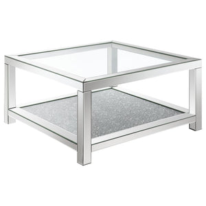 This glam mirrored coffee table is the epitome of Hollywood Regency vibes. Designed with beveled mirror trim and a tempered clear glass top, it offers modern flair and sophistication. The sparkling acrylic jewel-encrusted bottom shelf adds a dazzling touc