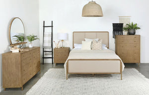 This coastal-inspired bedroom set blends mid-century modern influences with natural textures for a serene retreat. The bed features a cream fabric upholstered headboard and footboard, framed by a wire-brushed wood finish that enhances the beauty of rubber