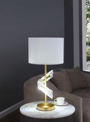  this pair of gold table lamps features a clean drum shade paired with sculptural acrylic accents that wrap around the slender frame. A brilliant LED light glows from within the swirling acrylic