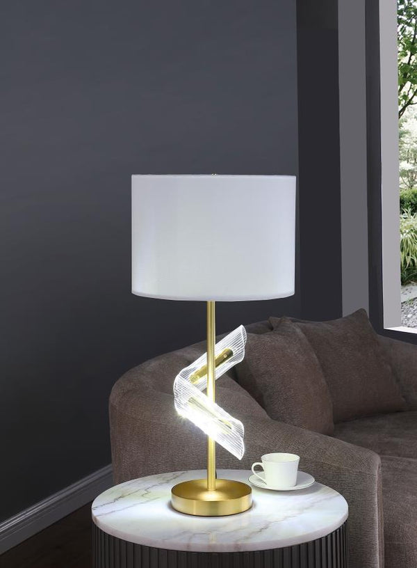  this pair of gold table lamps features a clean drum shade paired with sculptural acrylic accents that wrap around the slender frame. A brilliant LED light glows from within the swirling acrylic