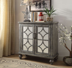 The transitional Velinka Console Table features a weather gray finish with mirrored glass doors and a diamond trim inlay. Two cabinet doors open on the rectangular wood console table to reveal ample shelf space for additional storage. The modern style cab