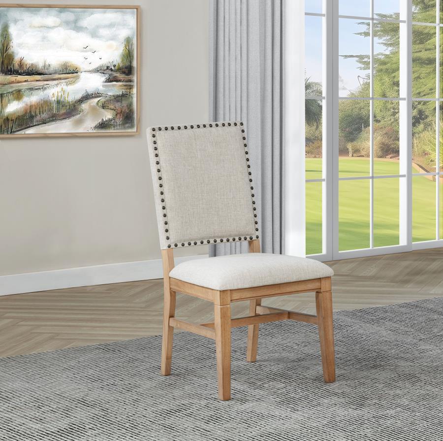 This refined dining side chair enhances any mealtime experience with subtle elegance. Upholstered in beige fabric, it features individually hand-driven black nailhead trim for artisanal detail. Crafted with a solid hardwood frame and legs in a natural bro