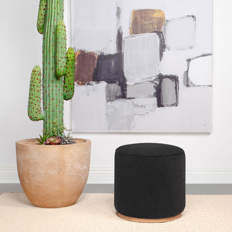 Add a touch of playful luxury to your living space with this round upholstered ottoman, swathed in sumptuous faux sheepskin that invites you to touch. Resting on a metal base that-'s been expertly finished to emulate the warm, natural allure of wood grain