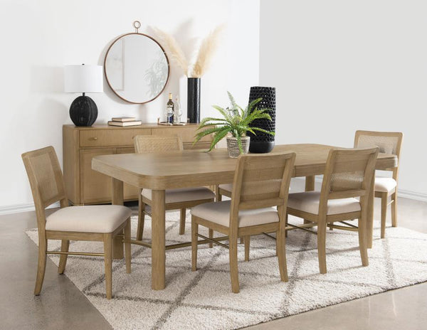 This dining set blends modern craftsmanship with natural textures for a refined yet inviting feel. The dining table features a trestle base with an antique brass-finished metal stretcher bar, adding stability and contrast. Rounded corners soften the recta