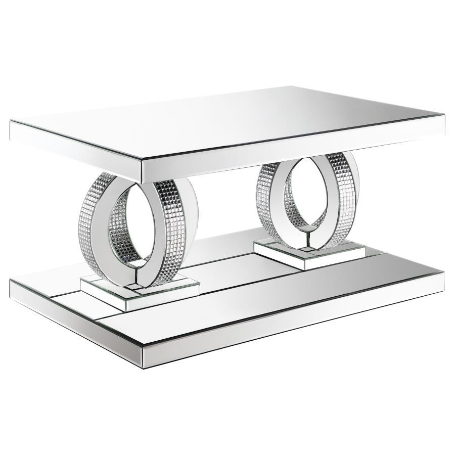 This glamorous mirrored coffee table captures the opulent spirit of Hollywood Regency design. Its base features interconnected dual rings adorned with dazzling acrylic crystals, while mirrored surfaces and softly beveled edges amplify its refined aestheti