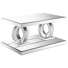 This glamorous mirrored coffee table captures the opulent spirit of Hollywood Regency design. Its base features interconnected dual rings adorned with dazzling acrylic crystals, while mirrored surfaces and softly beveled edges amplify its refined aestheti