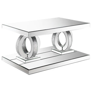 This glamorous mirrored coffee table captures the opulent spirit of Hollywood Regency design. Its base features interconnected dual rings adorned with dazzling acrylic crystals, while mirrored surfaces and softly beveled edges amplify its refined aestheti