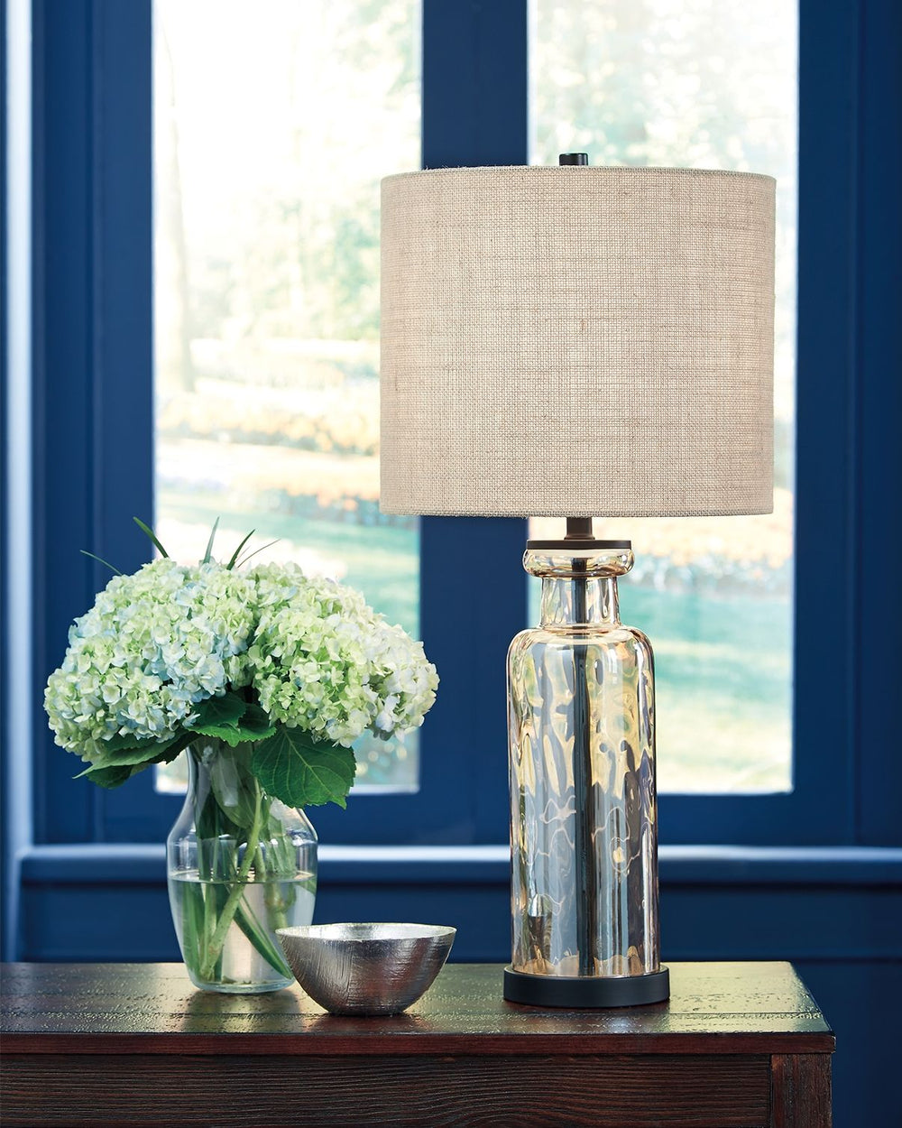 Transparency is in style with this table lamp. A unique pattern reflects in the faceted base as light passes through. Antique bronze-tone metal beautifully complements the champagne glass finish. Burlap shade adds texture to the smooth design.<br><br><b>A