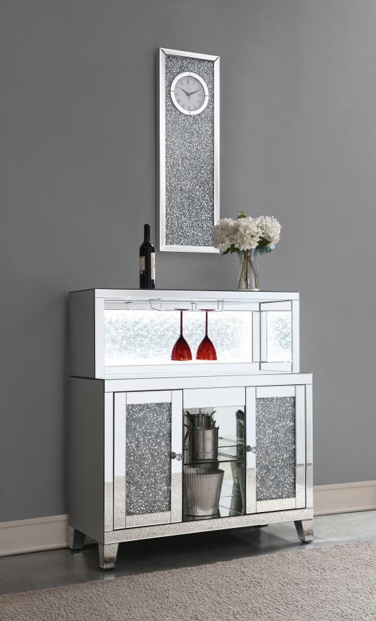 This wine cabinet is a striking statement piece that features a highly reflective surface made of mirror tiles and trim. The faux diamond encrusted doors and crystal knobs add a hint of sparkle while the open back shelf emits a soothing glow. This spaciou