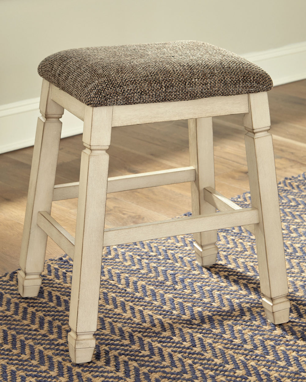The beauty of this upholstered bar stool is something to savor. Designed to serve up comfort and flair, this backless bar stool entices with a saddle seat covered in a heavy woven fabric that complements the antiqued white finish.<br><br><b>Additional Dim