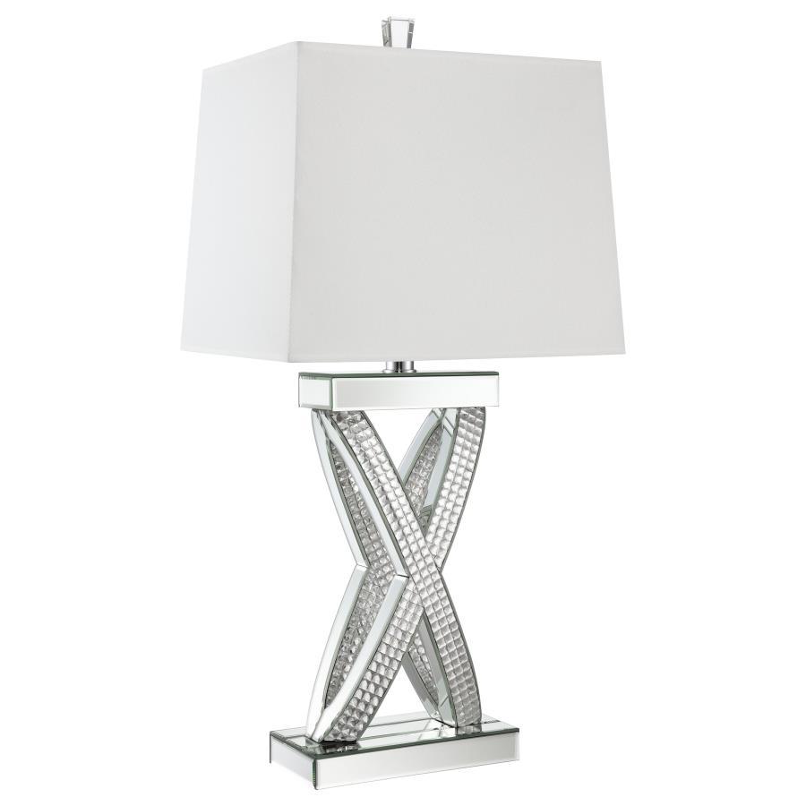 This table lamp features a sculptural X-shaped base accented with shimmering mirrored panels and faceted acrylic crystal inlays. Its bold silhouette and reflective finish create a dramatic presence, while a rectangular white shade provides soft ambient li