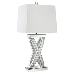 This table lamp features a sculptural X-shaped base accented with shimmering mirrored panels and faceted acrylic crystal inlays. Its bold silhouette and reflective finish create a dramatic presence, while a rectangular white shade provides soft ambient li