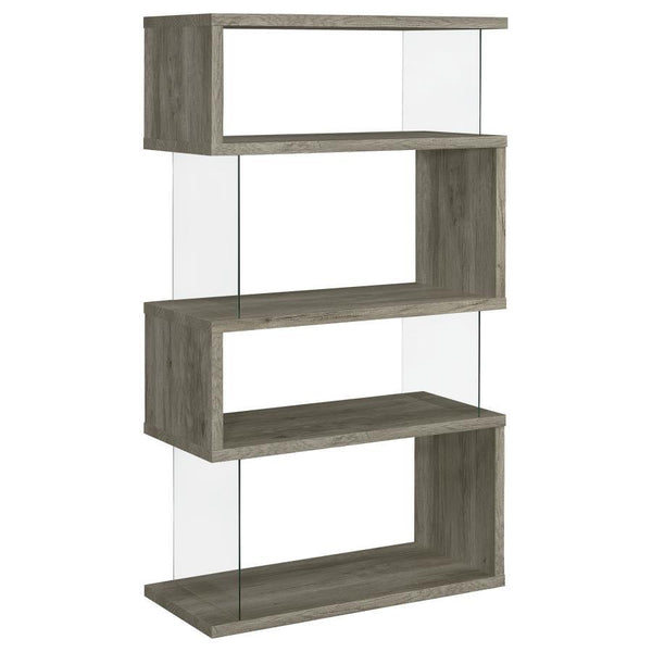 The asymmetrical zig-zag design of this contemporary bookcase creates a focal point in any room. Five open shelves in a light grey driftwood finish stack elegantly, supported by clear glass side panels that lend a modern flair to this furniture piece. Per