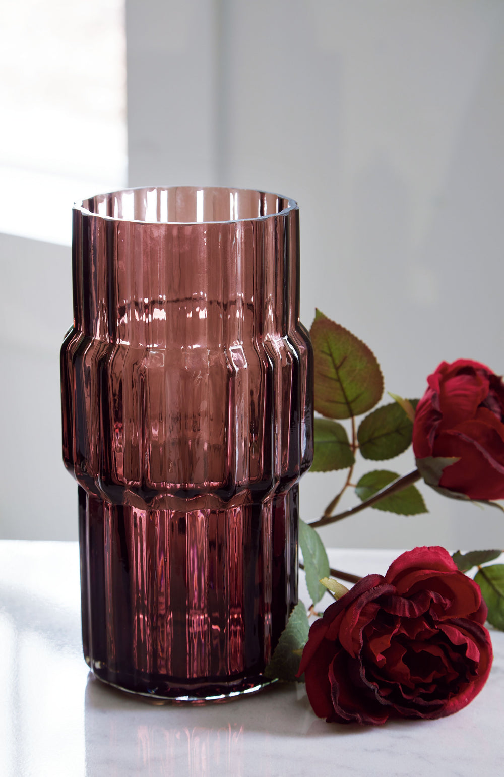This vase, made of dark mauve-tinted glass, adds a captivating touch to indoor or outdoor decor. Its unique textured shape and oversized fluted details create an elegant art piece. Whether it-'s accentuating flowers or candlelight, this vase is simply str