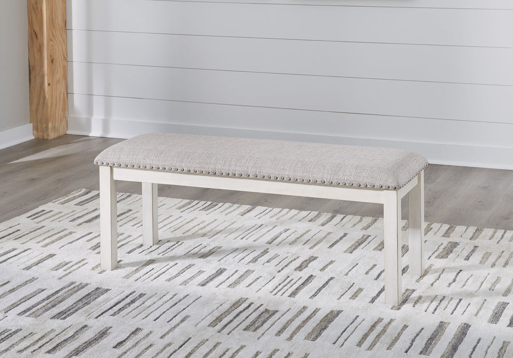 The Robbinsdale dining bench is sure to impress come mealtime. With its antiqued white finish and light gray upholstery with nailhead trim, modern farmhouse-style dining has never been so fashionable. All that-'s missing is you and your family.<br/><br/><