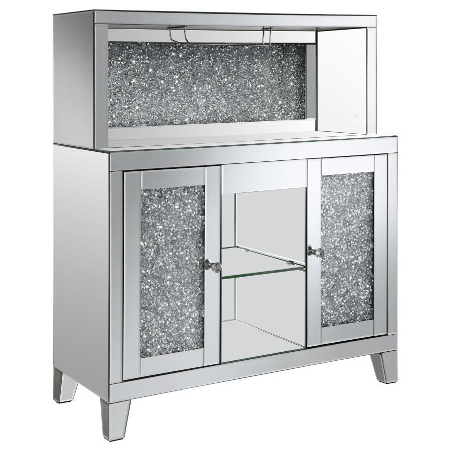 This wine cabinet is a striking statement piece that features a highly reflective surface made of mirror tiles and trim. The faux diamond encrusted doors and crystal knobs add a hint of sparkle while the open back shelf emits a soothing glow. This spaciou