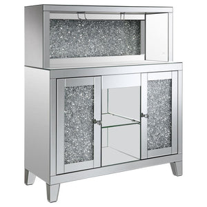 This wine cabinet is a striking statement piece that features a highly reflective surface made of mirror tiles and trim. The faux diamond encrusted doors and crystal knobs add a hint of sparkle while the open back shelf emits a soothing glow. This spaciou