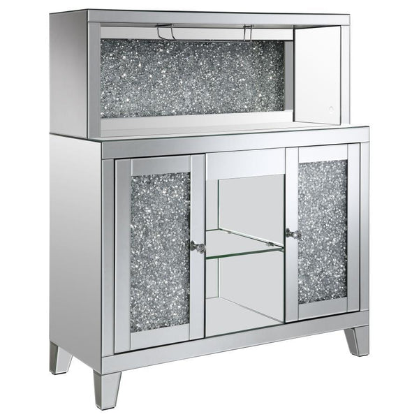 This wine cabinet is a striking statement piece that features a highly reflective surface made of mirror tiles and trim. The faux diamond encrusted doors and crystal knobs add a hint of sparkle while the open back shelf emits a soothing glow. This spaciou