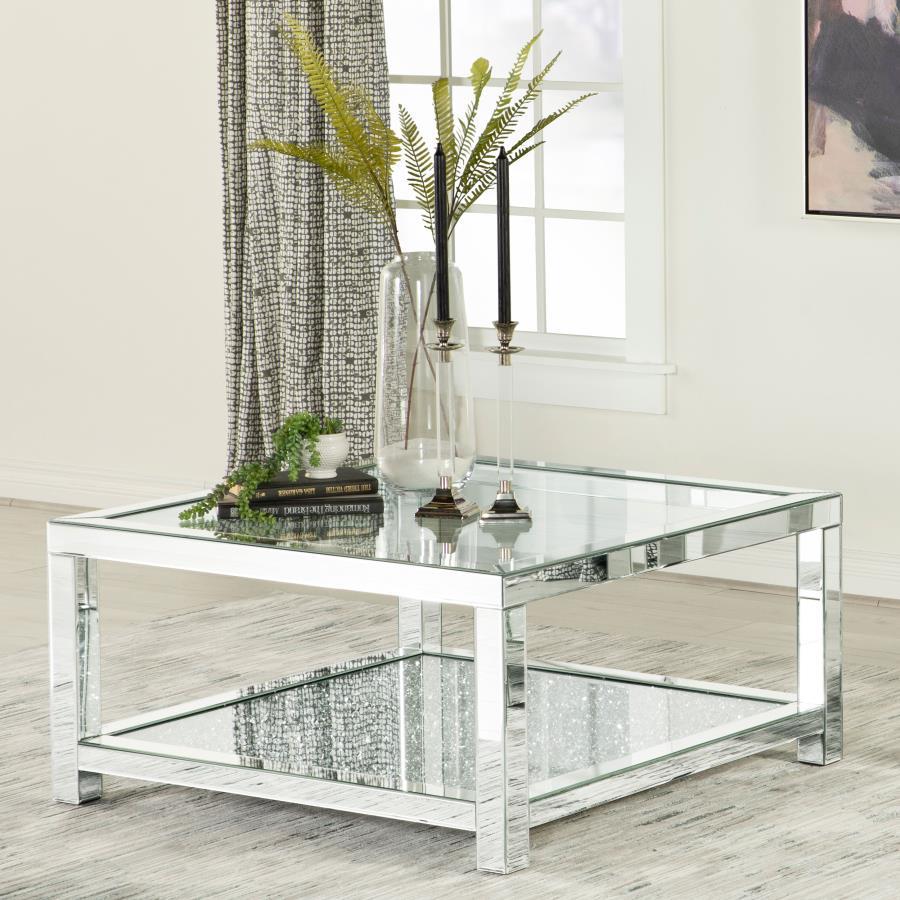 This glam mirrored coffee table is the epitome of Hollywood Regency vibes. Designed with beveled mirror trim and a tempered clear glass top, it offers modern flair and sophistication. The sparkling acrylic jewel-encrusted bottom shelf adds a dazzling touc