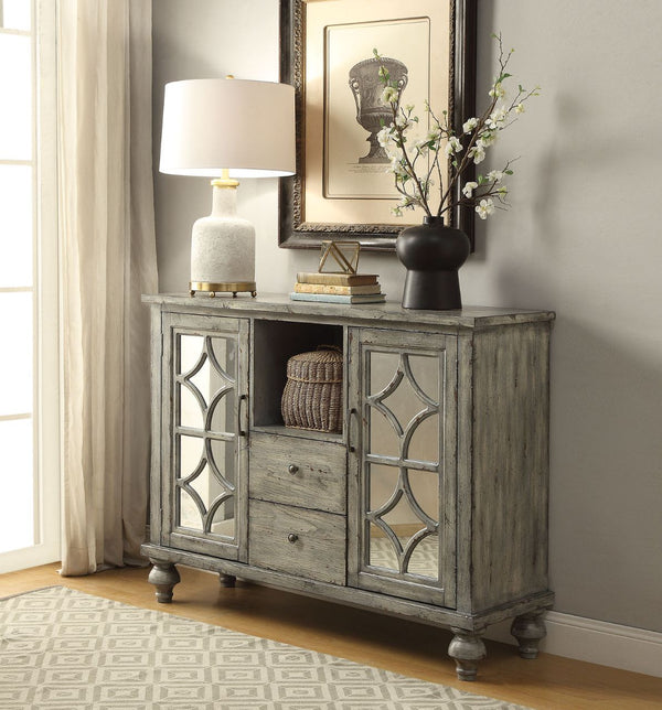 The transitional Velinka Console Table features a weather gray finish with mirrored glass doors and a diamond trim inlay. The wood console table features 2 storage doors, 2 storage drawers and one shelf providing ample display and additional storage space