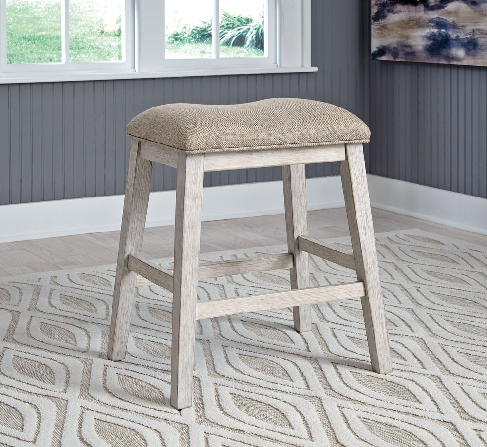 This upholstered stool invites you to raise the bar on small space living. An inspired choice for coastal chic or modern farmhouse settings, this comfortably cushioned stool sports a grayish white finish with rub-through effect for timeworn appeal.<br><br