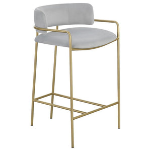 A soft and supple grey velvet envelops the comfy padded seat and linear backrest of this chic and glamorous stool. Situated and supported by a slim rod-like frame in a gold finish, this stool offers an air of sophistication to any bar top or kitchen islan