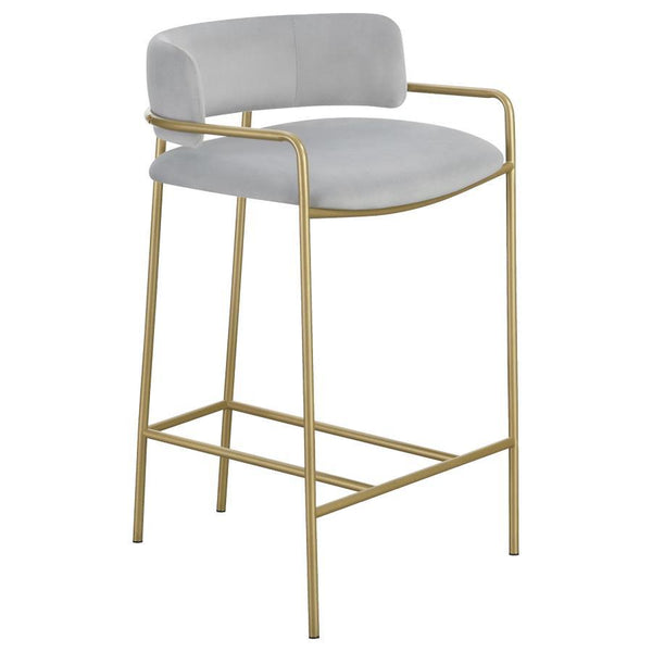 A soft and supple grey velvet envelops the comfy padded seat and linear backrest of this chic and glamorous stool. Situated and supported by a slim rod-like frame in a gold finish, this stool offers an air of sophistication to any bar top or kitchen islan