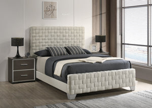 This bed is a statement piece that brings a touch of luxury and contemporary design to any bedroom setting. It features an oversized, padded headboard with a detailed basketweave pattern that adds texture and sophistication. The upholstery is crafted with