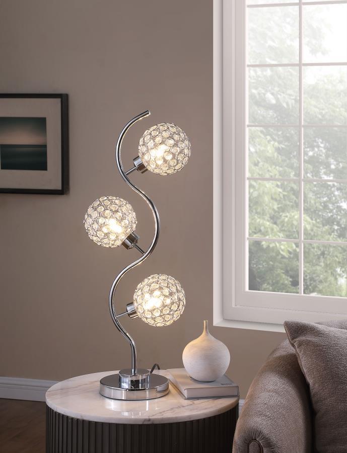 Sparkling with glamour, this modern three-light table lamp is a superb choice for a sophisticated living space. A corkscrew inspired post gleams in a chrome finish and hosts its three lights. Each features an orb shade dotted with crystal-like embellishme