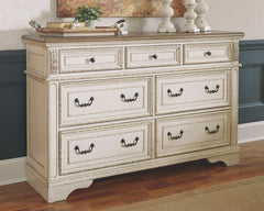 Elevating the art of traditional cottage styling, this dresser is your dream bedroom retreat realized. Its antiqued two-tone aesthetic blends a chipped white with a distressed wood finished top for added charm. Framed drawer fronts and decorative corbels 