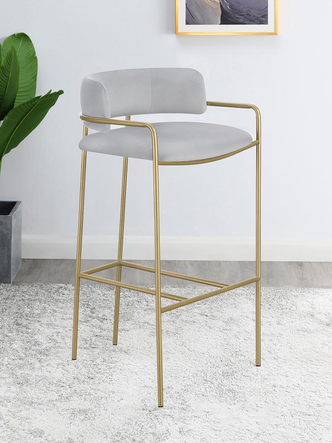A soft and supple grey velvet envelops the comfy padded seat and linear backrest of this chic and glamorous stool. Situated and supported by a slim rod-like frame in a gold finish, this stool offers an air of sophistication to any bar top or kitchen islan