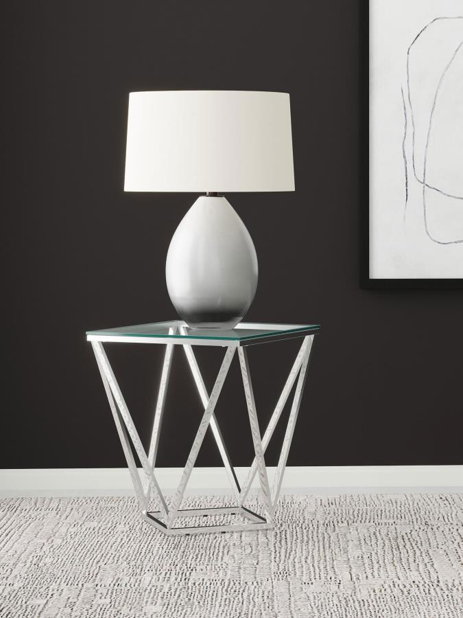 Simple geometric shapes combine to form a strikingly modern end table. The design features open, flared triangles in metal with a gleaming nickel finish, creating a dynamic base. A square glass top offers a smooth, airy surface, perfect for displaying dec