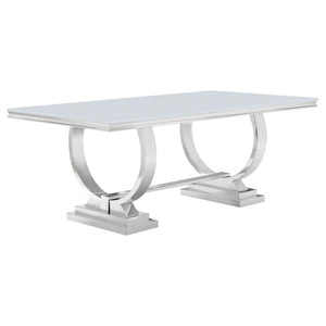 This modern dining table makes a bold statement with its sleek tempered glass top and sculptural stainless steel base. Designed for both elegance and durability, the spacious rectangular surface provides ample room for dining, while the curved trestle des
