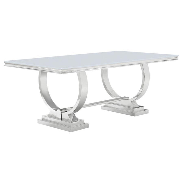 This modern dining table makes a bold statement with its sleek tempered glass top and sculptural stainless steel base. Designed for both elegance and durability, the spacious rectangular surface provides ample room for dining, while the curved trestle des
