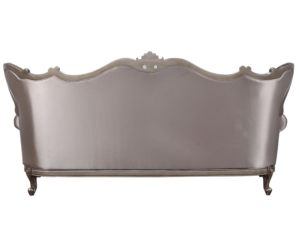 The Jayceon sofa collection is gorgeous, with shimmery fabric upholstery that highlights the champagne finish of the wooden frame. Button-tufted seatbacks wing out under carved arches. Loose seat cushions are upholstered in a floral patterned fabric that 