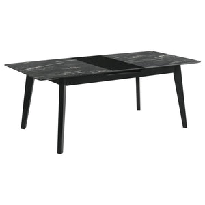 The luxurious look of faux marble creates a glam sensibility for a modern dining table. The black marble look of the tabletop complements a sleek base with fin-style legs and a recessed apron. The table includes a self-storing leaf for easy expansion to a