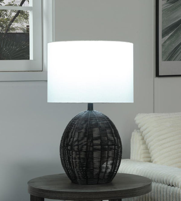  featuring a rounded black rattan base that adds visual intrigue. Paired with a sturdy metal frame for durability and a neutral fabric shade for soft